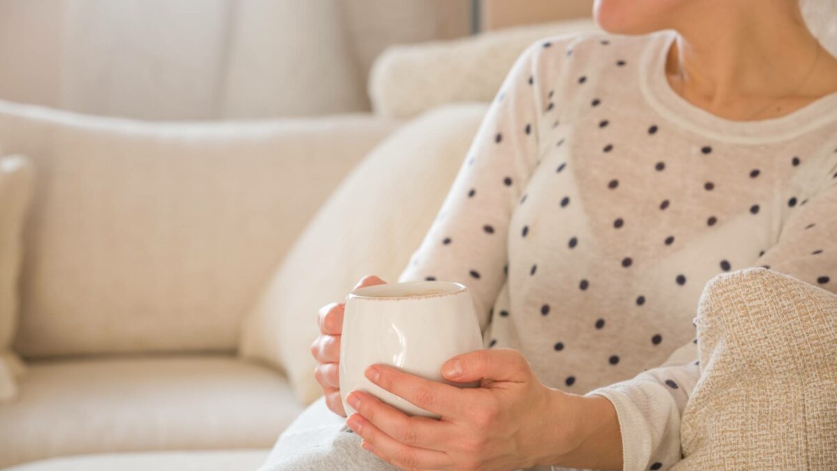 Dievča s hrnčekom kávy sediace na pohovke v interiéri. Žena pije šálku kávy alebo čaju a sedí pohodlne doma. Relaxujte a odpočívajte.