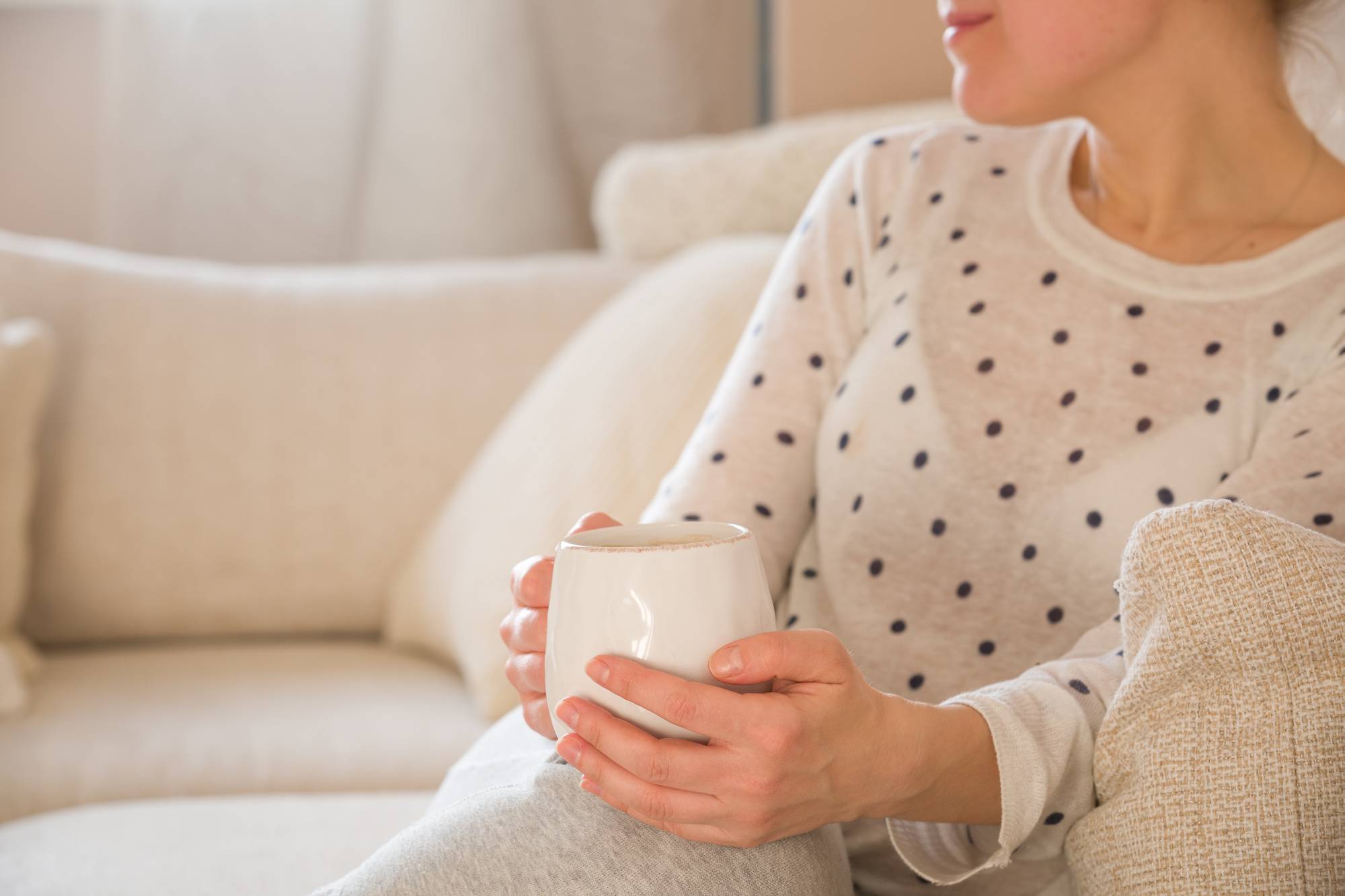 Tjej med kaffemugg som sitter på soffan inomhus. Kvinna som dricker en kopp kaffe eller te och sitter mysigt hemma. Koppla av och vila.