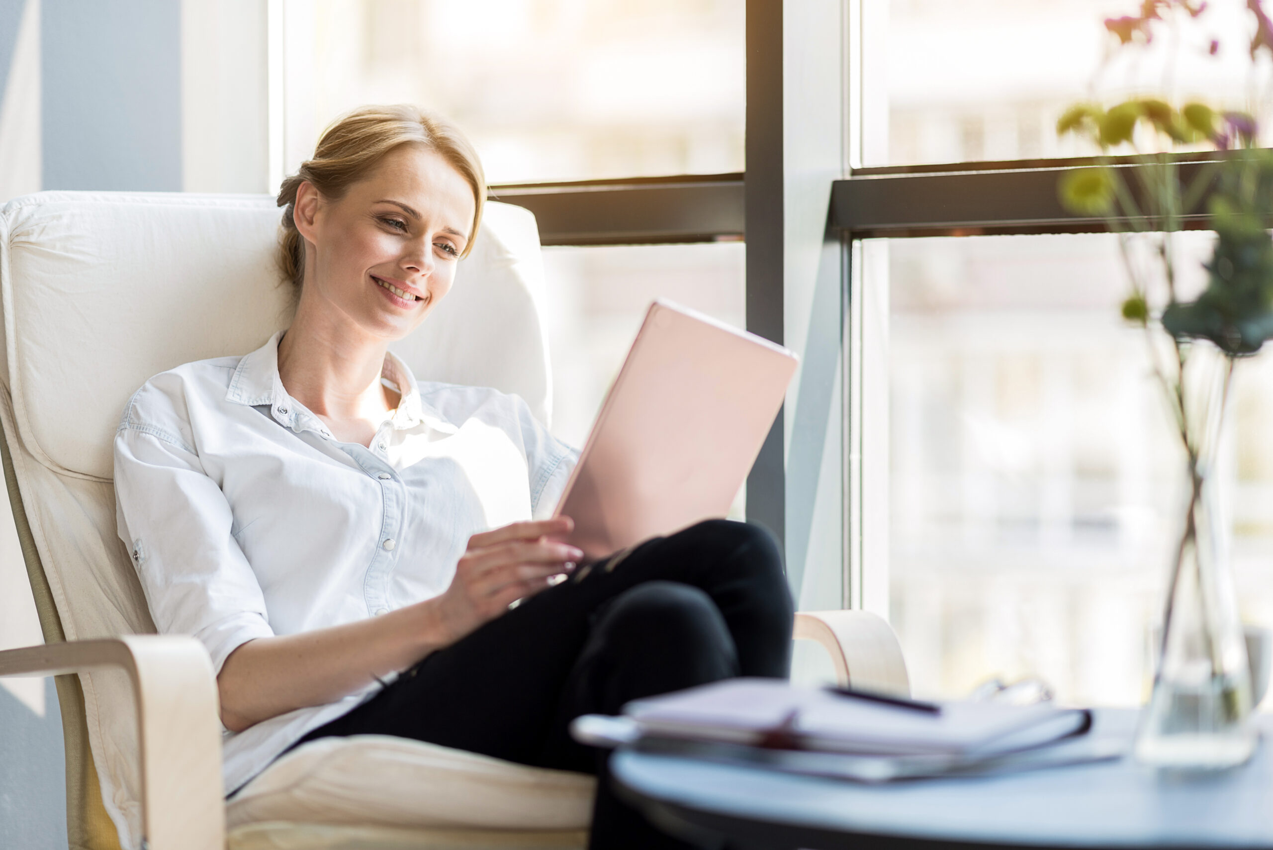 Comfort en plezier. De elegante positieve vrouw zit in grote comfortabele stoel terwijl het lezen van nieuws op tablet