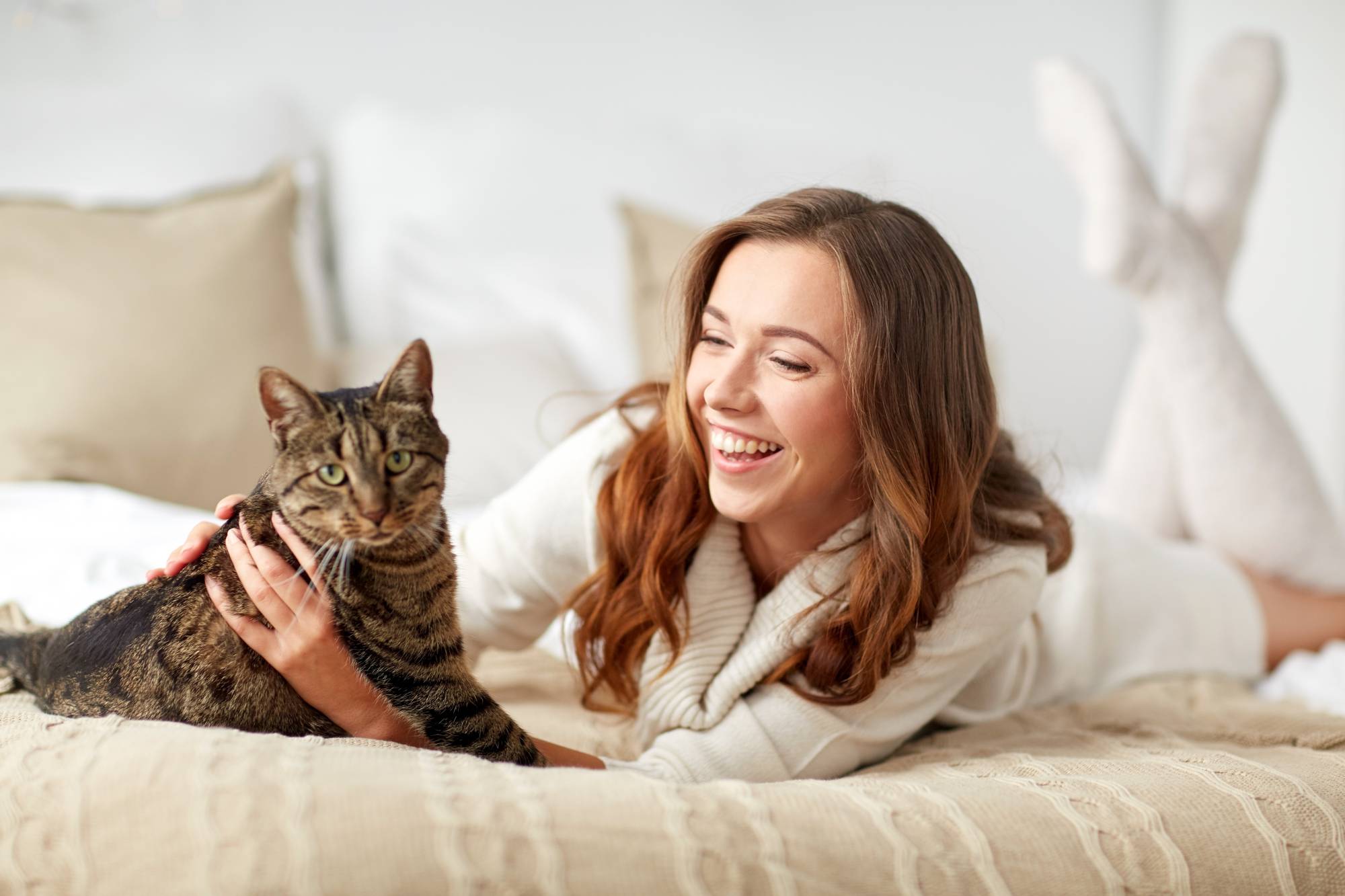 mascotas, comodidad, el descanso y el concepto de la gente - feliz mujer joven con gato acostado en la cama en casa